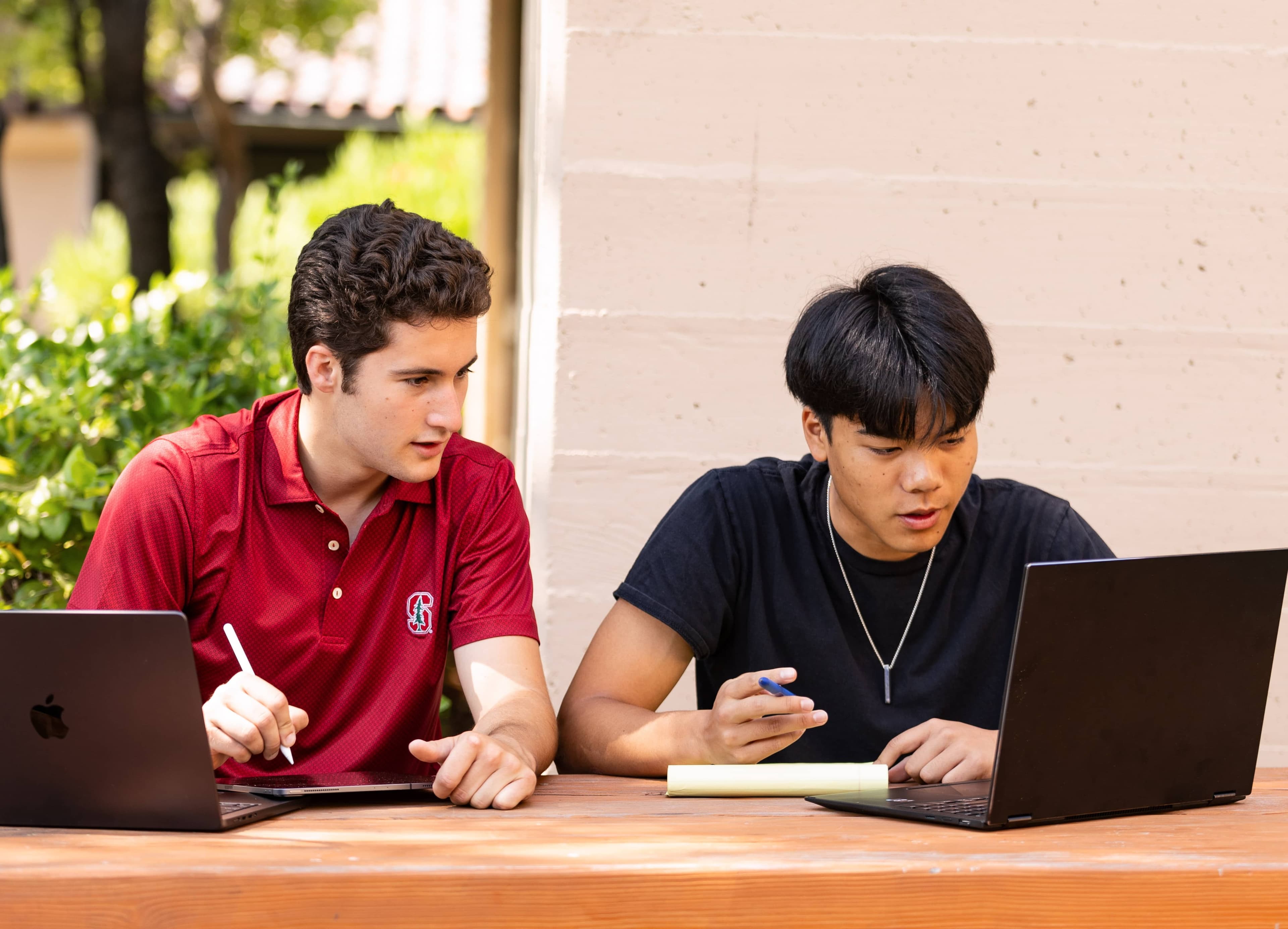 Students look at a laptop screen together outside at a table.
