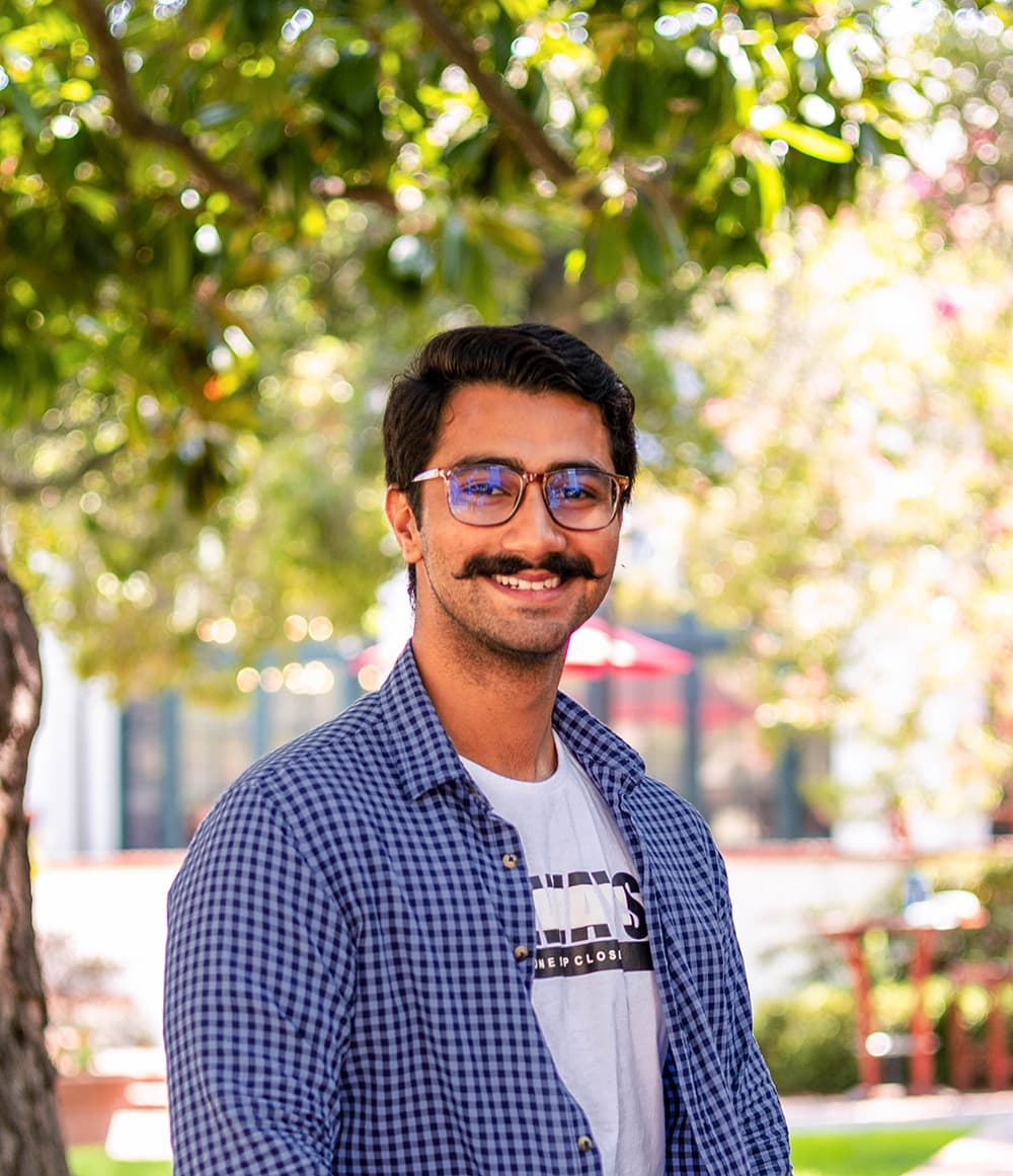 Ahmad wears a blue shirt and sits on a wall outside.