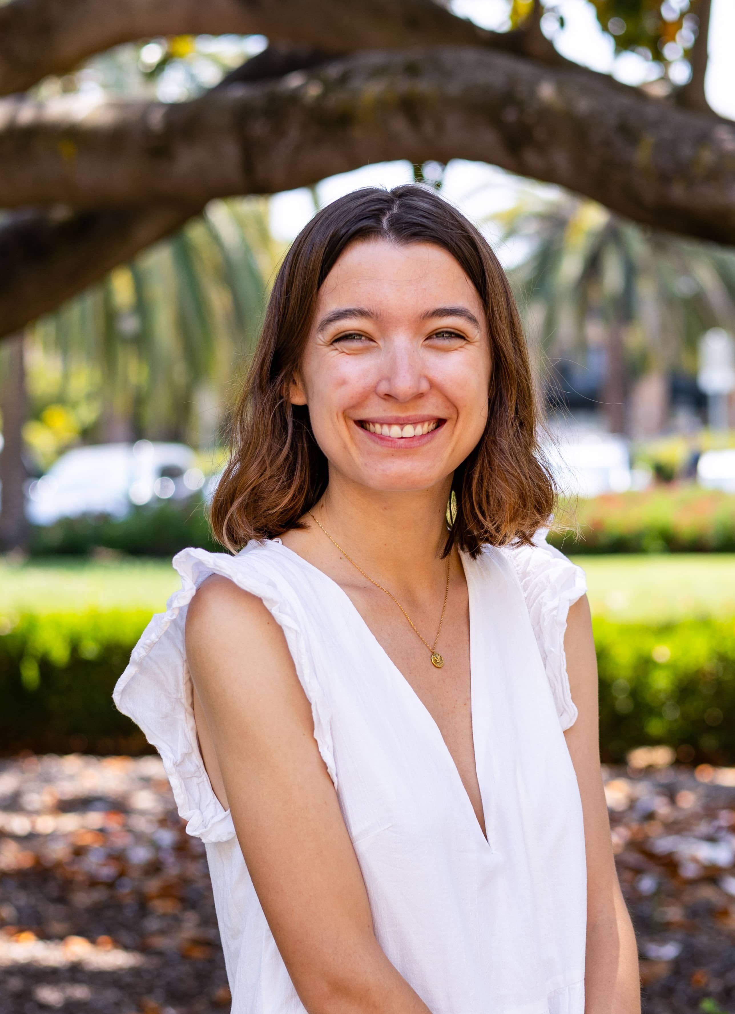 Jeanne sits under a tree in a white top.
