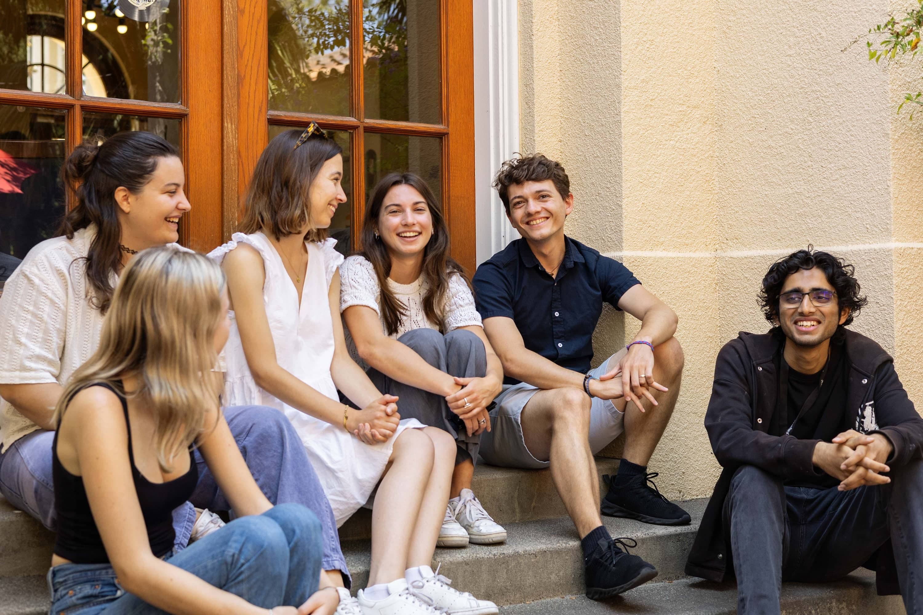 A group of students sit laughing on the steps. (Photo credits to Cayden Gu/Ethography for Stanford Summer Session)