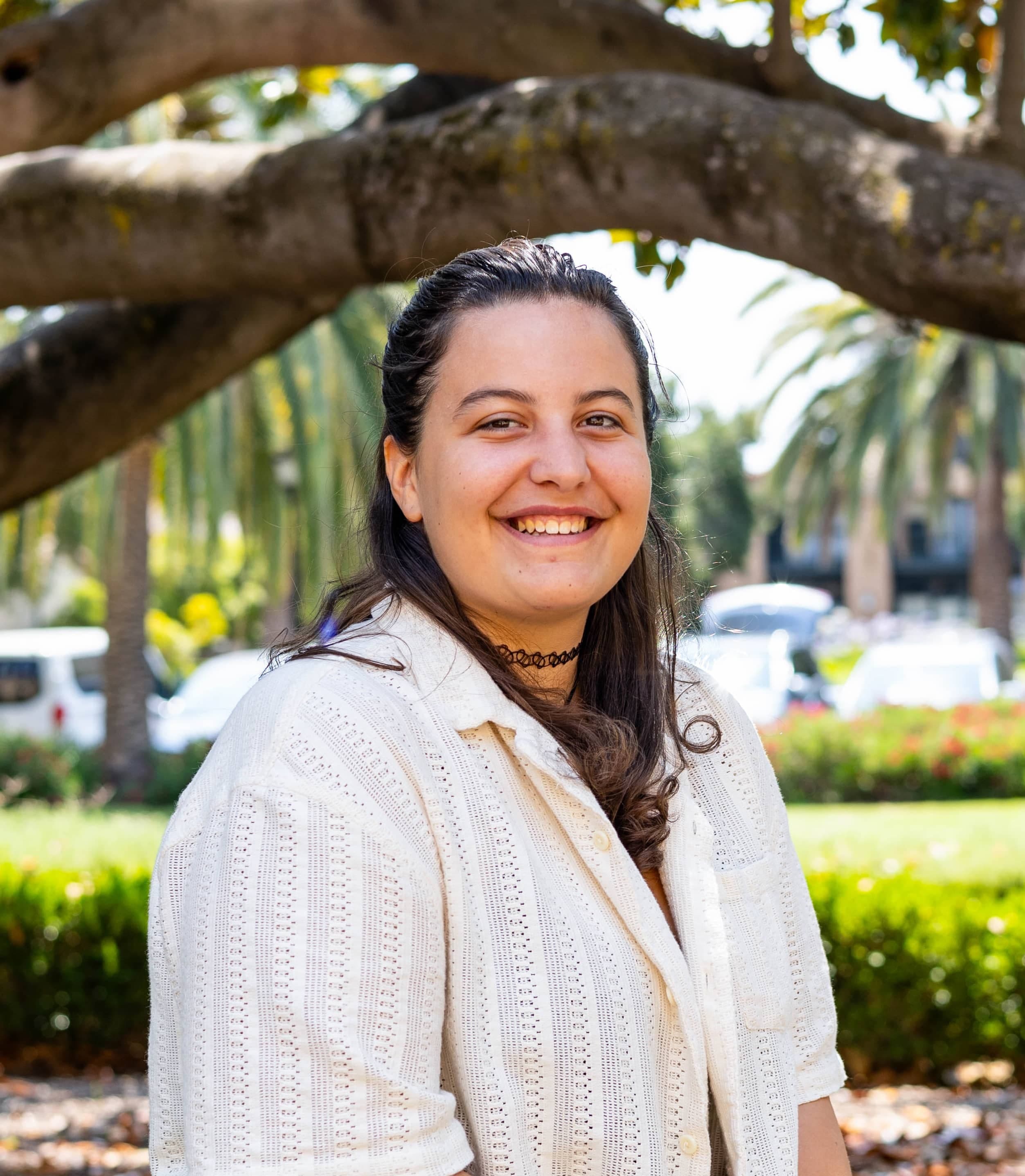 Ginny sits under a tree in a white shirt.